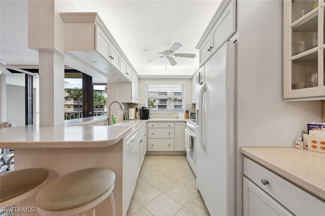 kitchen featuring white appliances, ceiling fan, light tile patterned floors, kitchen peninsula, and a breakfast bar area