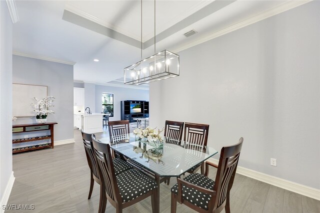 dining area with light wood-type flooring, an inviting chandelier, ornamental molding, and sink