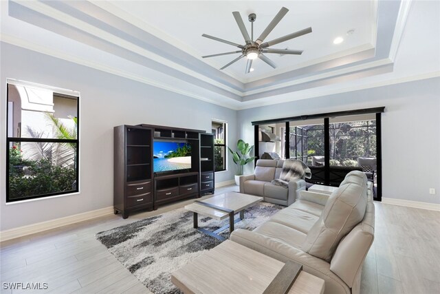 living room featuring a raised ceiling, ceiling fan, crown molding, and light wood-type flooring