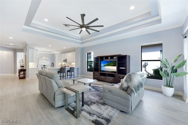 living room with light hardwood / wood-style flooring, a raised ceiling, ceiling fan, and ornamental molding