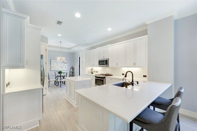 kitchen featuring kitchen peninsula, hanging light fixtures, light hardwood / wood-style flooring, appliances with stainless steel finishes, and white cabinetry