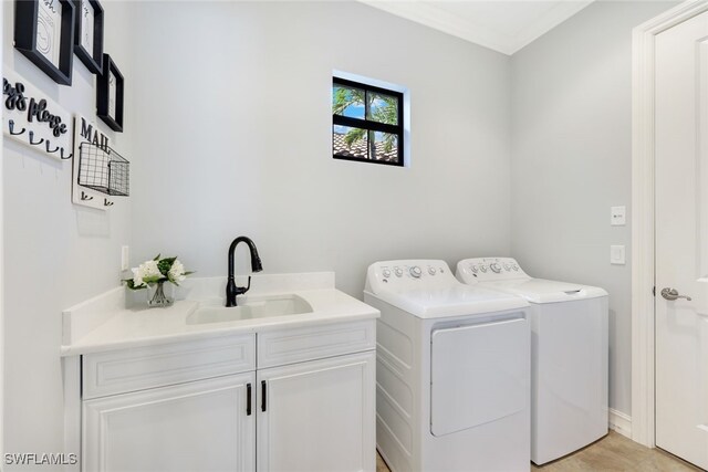 clothes washing area with washer and clothes dryer, crown molding, cabinets, and sink