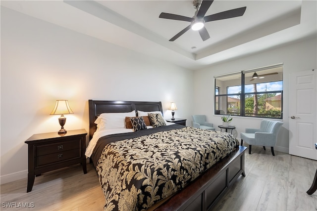 bedroom featuring ceiling fan, a raised ceiling, and light hardwood / wood-style flooring