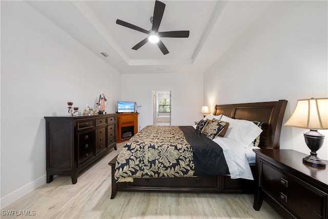 bedroom featuring ceiling fan, light wood-type flooring, and a tray ceiling