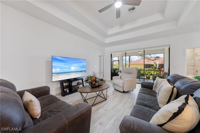 living room with ceiling fan, light hardwood / wood-style floors, a raised ceiling, and a towering ceiling