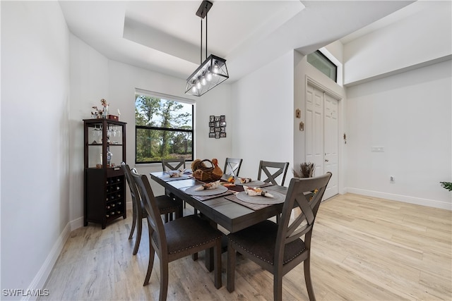 dining room with light wood-type flooring, a raised ceiling, and a notable chandelier