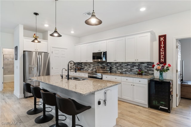 kitchen featuring white cabinetry, sink, stainless steel appliances, pendant lighting, and a kitchen island with sink