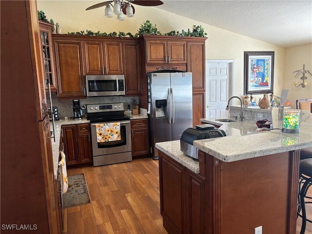 kitchen with a breakfast bar, lofted ceiling, light wood-type flooring, appliances with stainless steel finishes, and tasteful backsplash