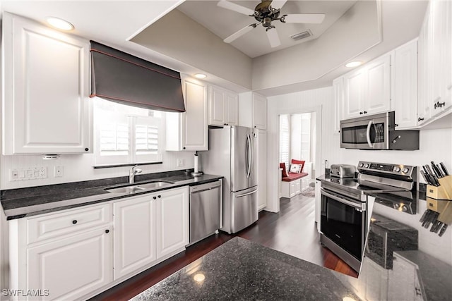 kitchen featuring appliances with stainless steel finishes, ceiling fan, sink, dark stone countertops, and white cabinetry