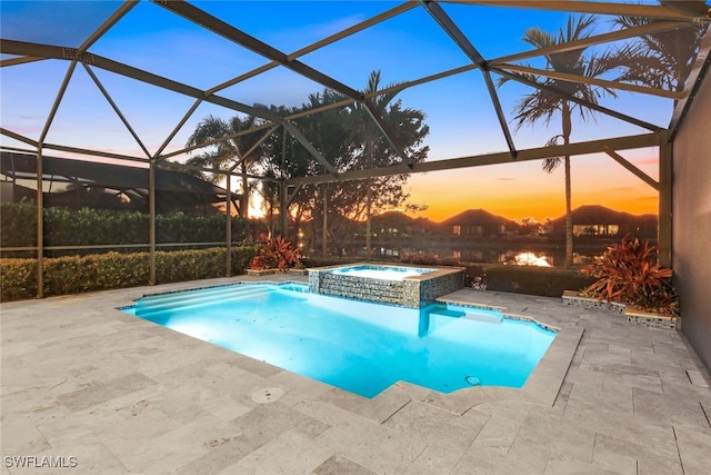 pool at dusk featuring glass enclosure, a patio area, and an in ground hot tub