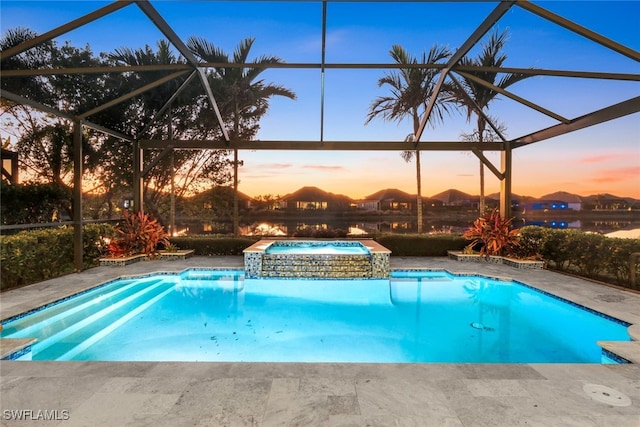 pool at dusk with a lanai and an in ground hot tub