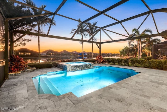 pool at dusk featuring glass enclosure, an in ground hot tub, and a patio