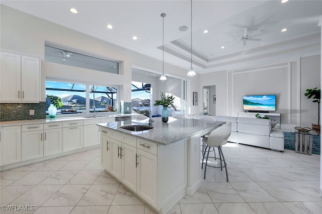 kitchen with sink, light stone counters, backsplash, a kitchen island with sink, and white cabinets