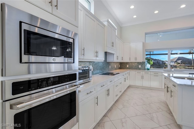 kitchen with appliances with stainless steel finishes, tasteful backsplash, light stone counters, crown molding, and white cabinets