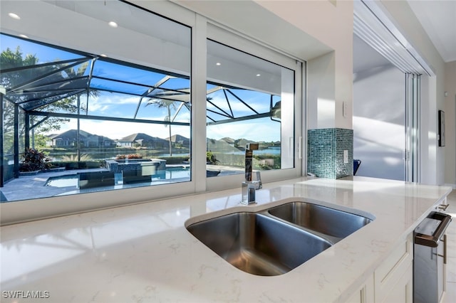 kitchen featuring plenty of natural light, white cabinetry, light stone countertops, and sink