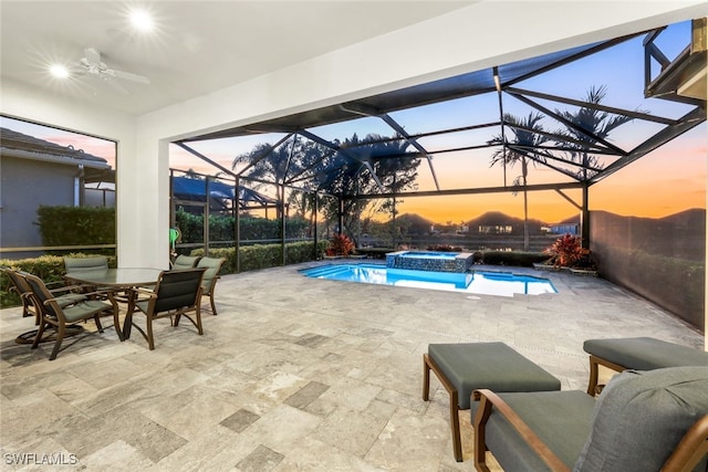 pool at dusk featuring an in ground hot tub, a patio, glass enclosure, and ceiling fan