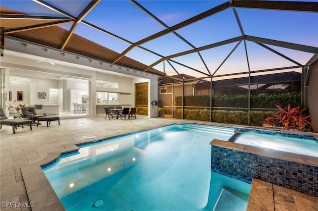 pool at dusk featuring a patio, an outdoor hangout area, glass enclosure, and ceiling fan