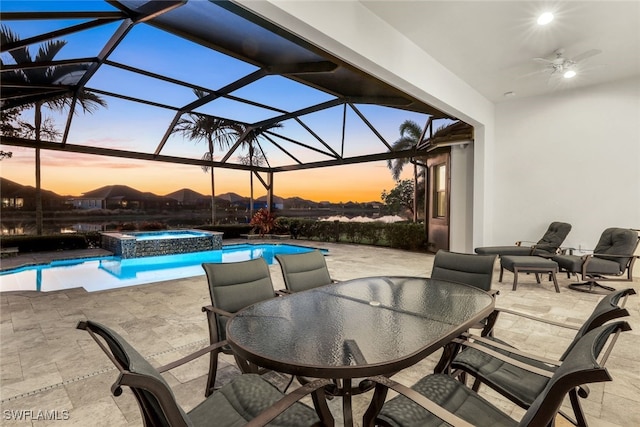 patio terrace at dusk with glass enclosure, ceiling fan, and a swimming pool with hot tub