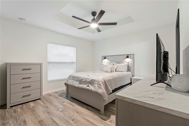 bedroom featuring ceiling fan, light hardwood / wood-style floors, and a tray ceiling