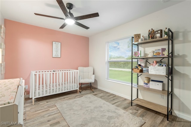 bedroom with a nursery area, hardwood / wood-style flooring, and ceiling fan