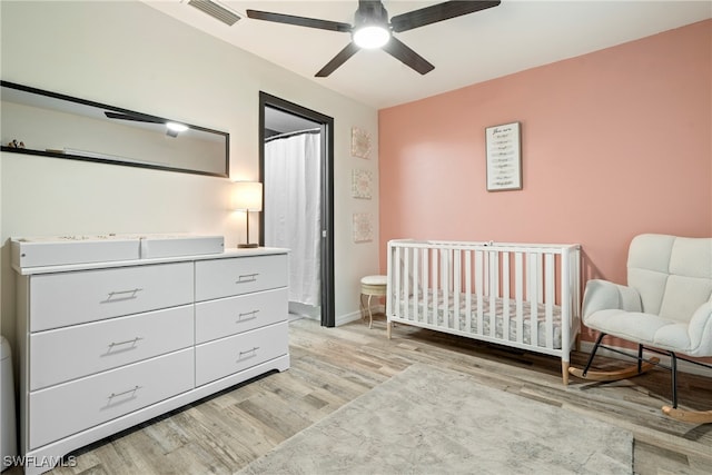 bedroom featuring ceiling fan, light hardwood / wood-style floors, and a crib