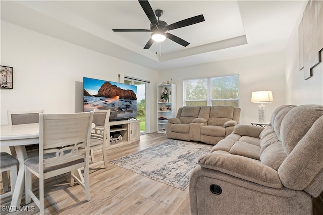 living room with hardwood / wood-style flooring, a raised ceiling, and ceiling fan