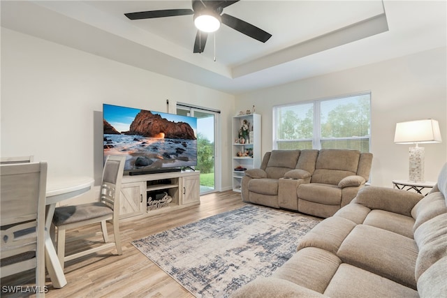 living room with a raised ceiling, ceiling fan, and wood-type flooring