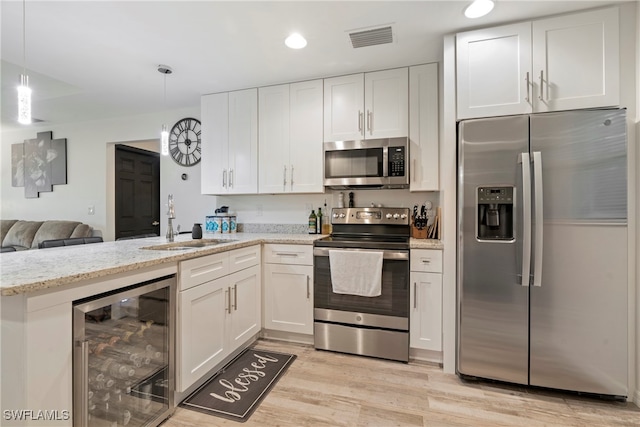 kitchen with white cabinetry, hanging light fixtures, wine cooler, appliances with stainless steel finishes, and light wood-type flooring