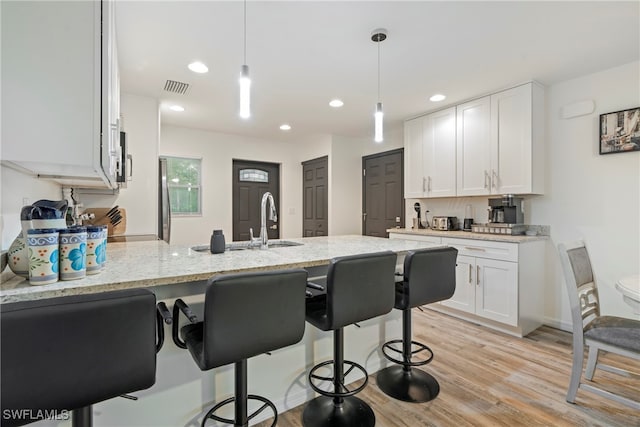 kitchen with light stone countertops, kitchen peninsula, light hardwood / wood-style flooring, white cabinets, and hanging light fixtures