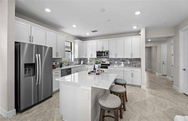 kitchen with a breakfast bar, sink, appliances with stainless steel finishes, a kitchen island, and white cabinetry