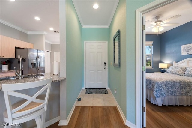 interior space with stainless steel fridge with ice dispenser, wood finished floors, ornamental molding, light stone countertops, and baseboards