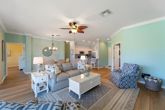 living area with baseboards, visible vents, ornamental molding, wood finished floors, and ceiling fan with notable chandelier