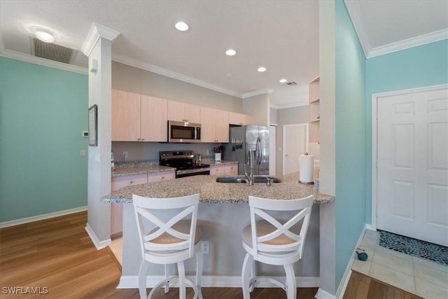 kitchen with a breakfast bar area, a peninsula, a sink, visible vents, and appliances with stainless steel finishes