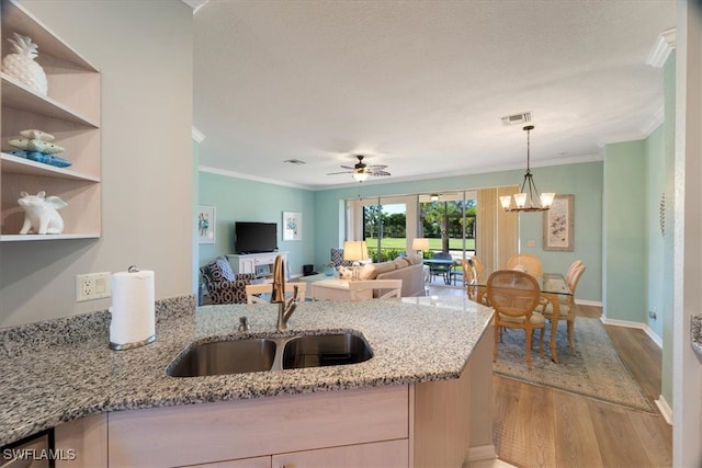 kitchen with ceiling fan with notable chandelier, light wood-type flooring, light stone countertops, and sink