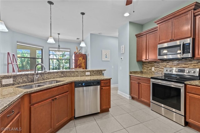 kitchen with sink, stainless steel appliances, tasteful backsplash, light stone counters, and decorative light fixtures