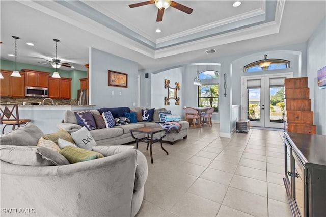 living room featuring ceiling fan, french doors, a raised ceiling, light tile patterned floors, and ornamental molding