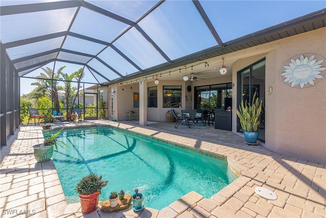 view of swimming pool with glass enclosure, ceiling fan, and a patio