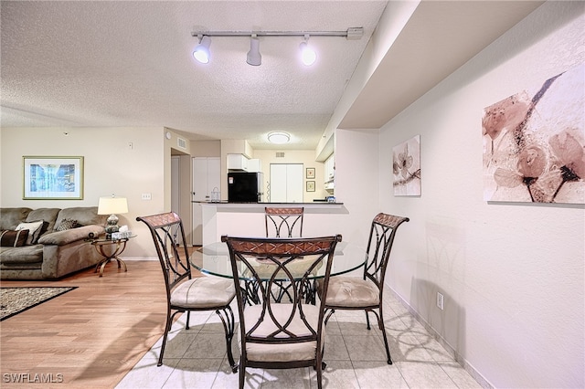 dining area featuring light wood-type flooring, a textured ceiling, and track lighting