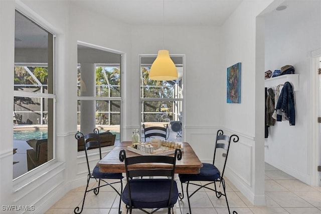 dining area with light tile patterned floors, wainscoting, and a decorative wall