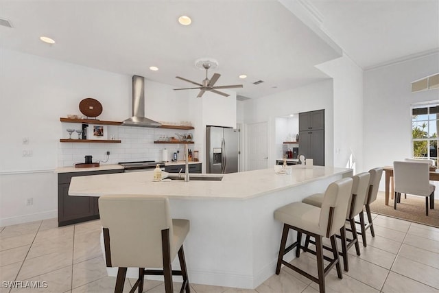 kitchen with wall chimney range hood, decorative backsplash, appliances with stainless steel finishes, and a large island with sink