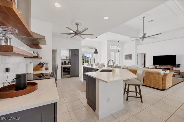 kitchen featuring light tile patterned floors, sink, ventilation hood, an island with sink, and wine cooler