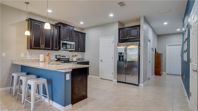 kitchen with stainless steel appliances, tasteful backsplash, light stone counters, decorative light fixtures, and a breakfast bar