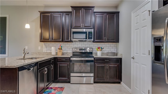 kitchen featuring kitchen peninsula, light stone counters, stainless steel appliances, sink, and pendant lighting