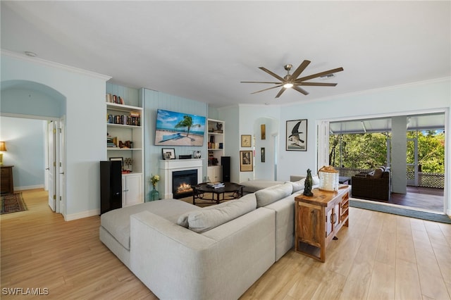 living room featuring ceiling fan, light wood-type flooring, crown molding, and built in shelves