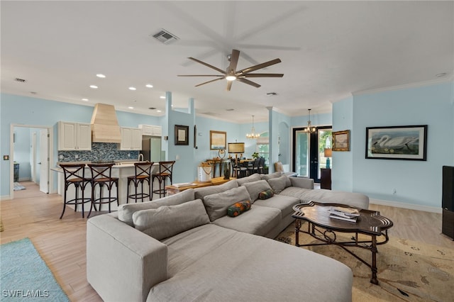 living room featuring french doors, light hardwood / wood-style floors, ceiling fan with notable chandelier, and ornamental molding