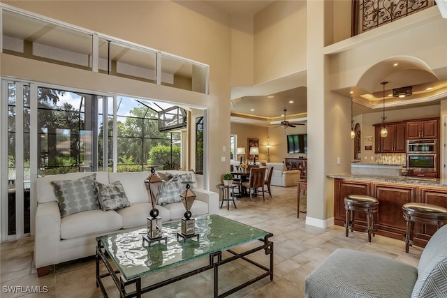 living room with ceiling fan, a towering ceiling, and crown molding