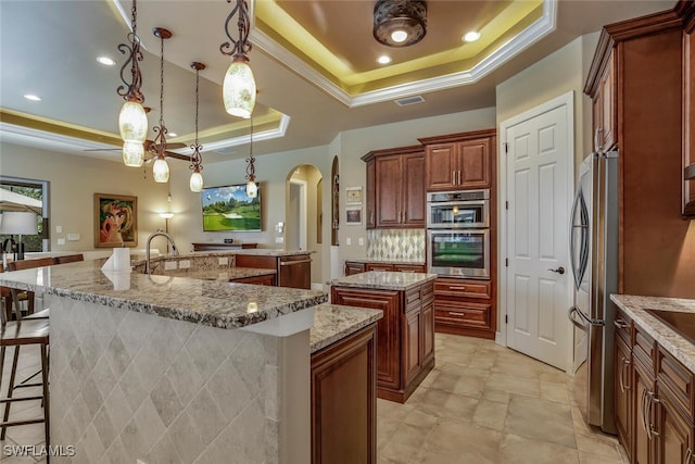 kitchen featuring stainless steel appliances, a raised ceiling, a spacious island, decorative light fixtures, and a breakfast bar