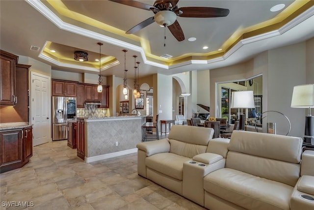 living room featuring a tray ceiling, ceiling fan, and crown molding