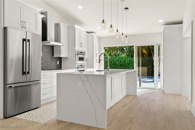 kitchen with wall chimney exhaust hood, white cabinetry, an island with sink, and appliances with stainless steel finishes