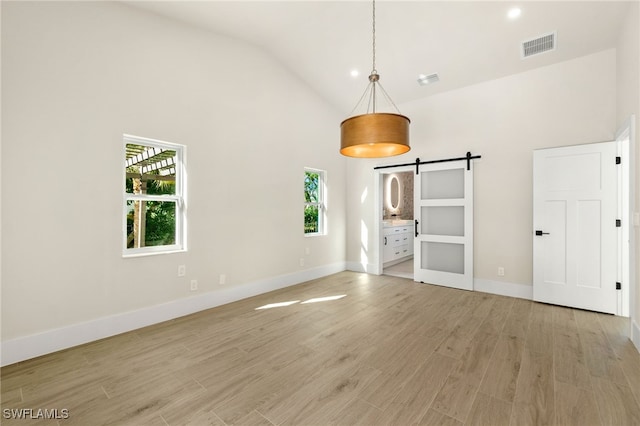 unfurnished living room featuring a barn door, plenty of natural light, high vaulted ceiling, and light wood-type flooring